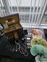 Overview of open jewelry box, assorted jewelry, fans and tins on table