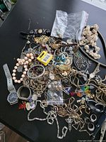 Top view of entire mixed jewelry pile with watches, pins, lipstick tube and battery pack visible