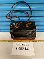 Full view of Roveri black body brown base handbag with strap and ruler for scale