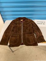 Full view of brown suede jacket laid flat showing overall design, pockets, collar