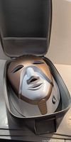Mask seated inside open grey case showing bronze front panel and overall appearance