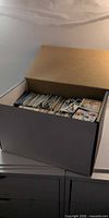 Open cardboard long box filled with rows of trading cards