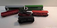 Group of six model train cars: two green CP Rail boxcars, black Canadian Pacific hopper, red CN gondola, two red CN cabooses