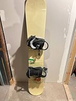 Full view of snowboard standing upright showing both bindings and graphics