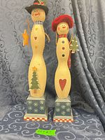 Front view of both wooden snowman figurines on patterned backdrop