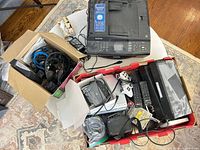 Overview showing Brother printer, two boxes of electronics including DVD player, remotes, controllers and cables