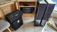 Full lot showing receiver, CD player in cabinet, remotes on shelf, subwoofer, center speaker, and two tower speakers