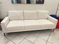 Full front view of light beige three-seat sofa showing cushions and legs