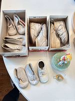 Overview of four pairs of white toddler shoes, three in Bonnie Stuart boxes, one pair loose, with ceramic cat music box
