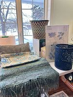 Overall lot showing throw, pillow cover, placemats, woven basket, IKEA panel box, metal wastebasket