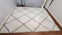 Full view of 8' x 10' white/cream shag rug with gray diamond pattern on hardwood floor