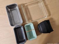 Top view of five items: glass dish, two loaf pans, small green pan, black pads