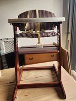 Front view of wooden high chair showing tray, cushion, harness and footrest