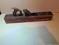 Left side view of full length wooden hand plane showing tote, wedge, and sole