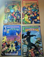 Front covers of Strangers issues 2, 3, 5, 6 displayed on cardboard background