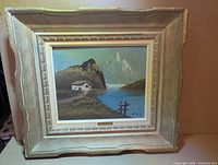 Front view of framed oil painting depicting mountain chalet, shows frame style and artist signature
