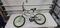 Full view of silver BMX-style bike on table showing green rims and overall condition