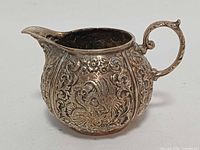 Front view of silverplated creamer with ornate repousse design and spout visible