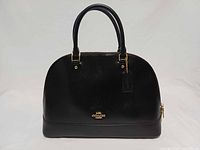 Front view of black Coach Sierra satchel showing patent finish, gold logo, rolled handles, hangtag