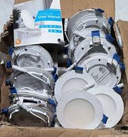 Box containing multiple white round LED recessed lights with wiring and junction boxes