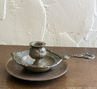 Side view of brass chamberstick resting on underplate showing handle detail and patina