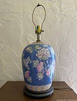 Full view of ginger jar lamp showing porcelain body, harp, brass hardware and wood base