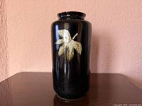 Front view of black glazed porcelain vase with beige leaf design