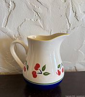 Front view of white ceramic pitcher with cherry motif