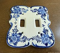 Front view of porcelain double switch cover showing blue floral pattern and mounting holes