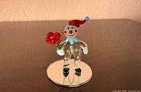 Front view of glass clown figurine holding red flower on mirrored base