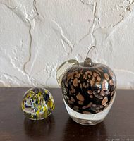 Murano apple paperweight beside round ribbon paperweight front view