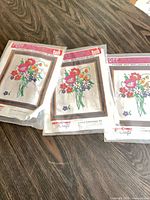 Three sealed crewel embroidery kits on tabletop