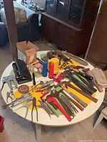 Overall view of assorted hand tools, flashlights, hardware and gloves on round table