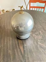 Chrome domed lid with brass finial resting on pedestal base