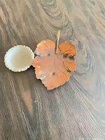 Copper leaf tray alongside milk glass bowl on wood surface