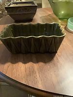 Rectangular scalloped ribbed green ceramic planter foreground, square planter background