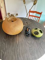Tan woven plastic pendant lamp, green hanging holder, wiring and chain on table