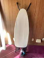 Ironing board standing vertically with cover visible, iron at base