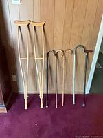Two wooden underarm crutches beside four canes