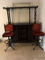 Full view of bar cabinet with metal scrollwork top and two red velvet bar stools