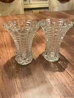 two matching clear pressed glass vases standing side by side on wooden surface