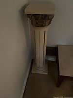 Full view of cream plaster pedestal column beside wall