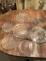 Eight assorted clear pressed glass plates on table