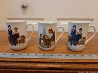 Front view of three mugs with Rockwell scenes, ruler for scale