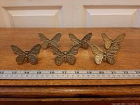 Front view of six brass butterfly napkin rings aligned with ruler for scale