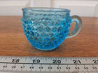 Side view of blue hobnail pressed glass cup with ruler for scale