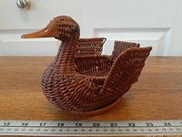 Left profile of brown wicker duck basket showing wooden beak and body weave with ruler for scale