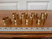 Eight brass napkin rings lined up with ruler for scale
