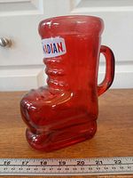 Side view of red glass skate-shaped mug showing handle and logo