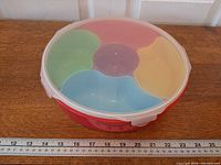 Top view showing red base, five colored compartments, latch lid, ruler for scale